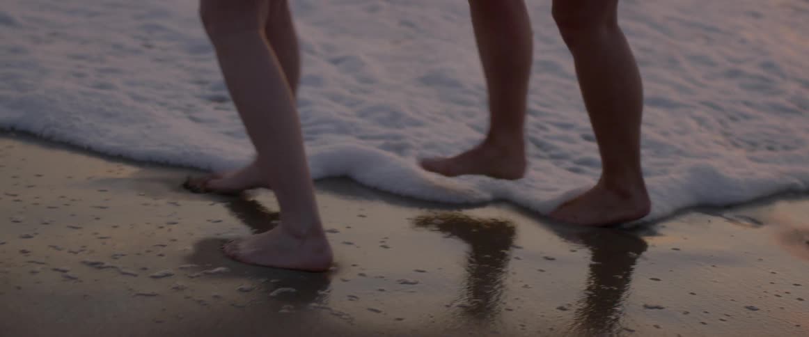 The two people walk in the water by the shore