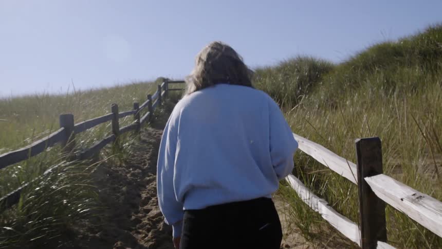 Woman walks on a trail lined with a wooden fence