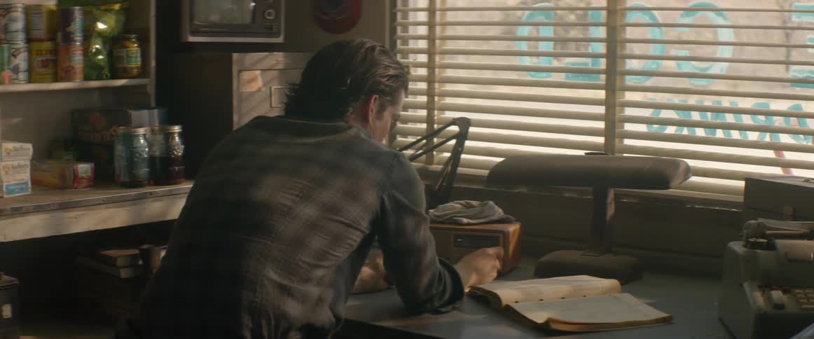 The man leans against the counter using a radio