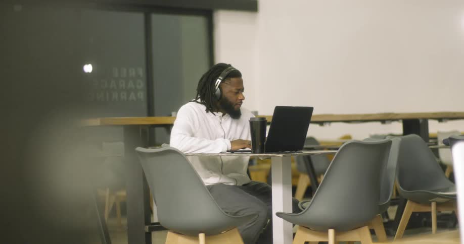 The man wears headphones using his laptop