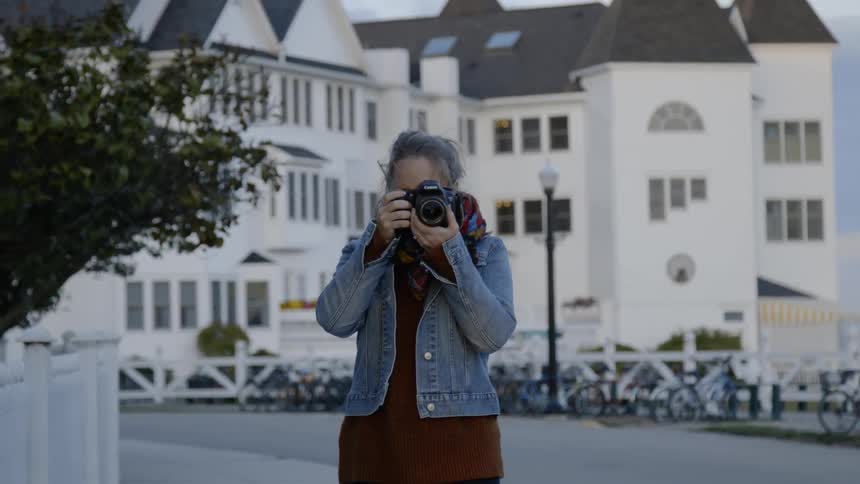A woman takes a photograph on a sidewalk