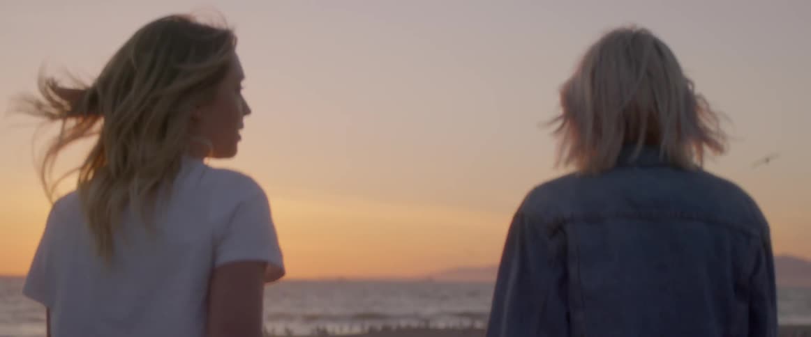 Two women walk on the beach at sunset