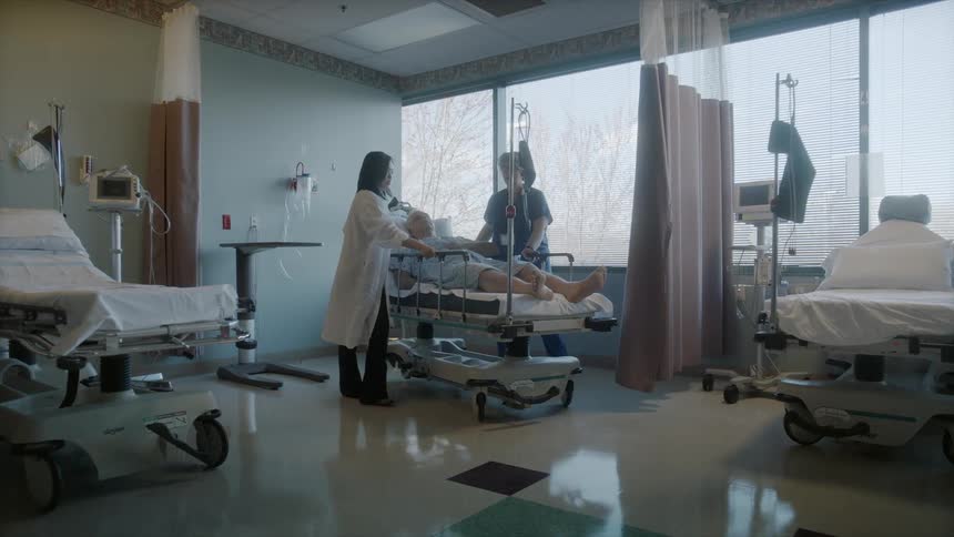 A female doctor and a female nurse wheeling a man in a hospital bed out of the room