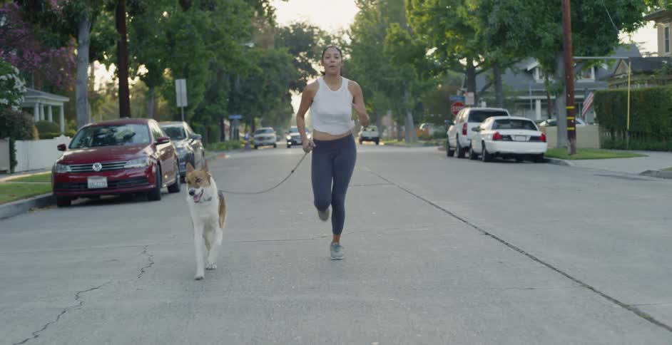 Smiling woman jogs down the street with her dog