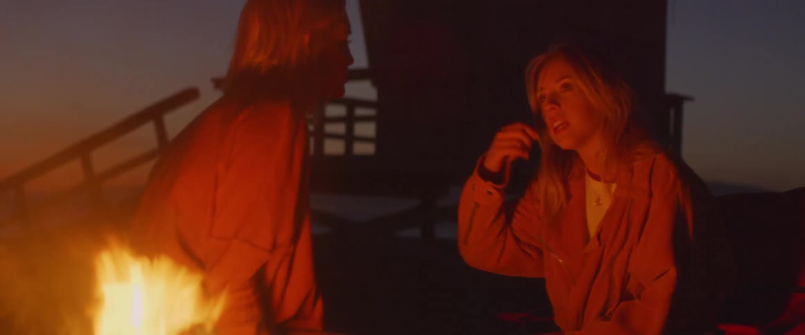 The two women talk by the campfire on the beach