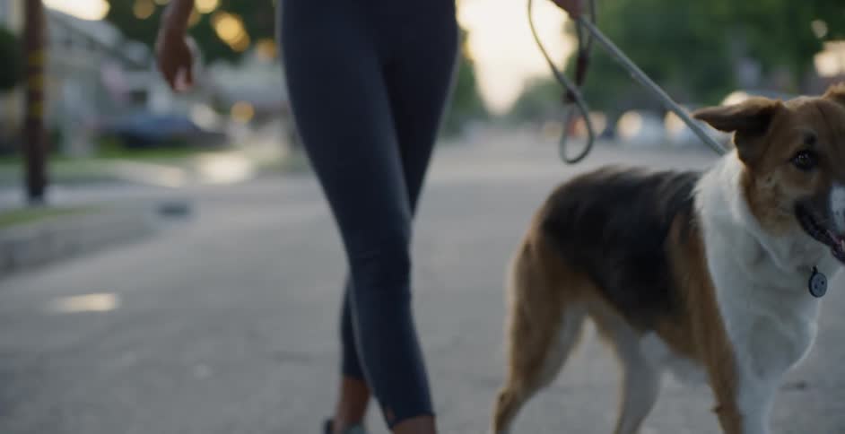 Woman in leggings walks on the street as she holds her dog on a leash