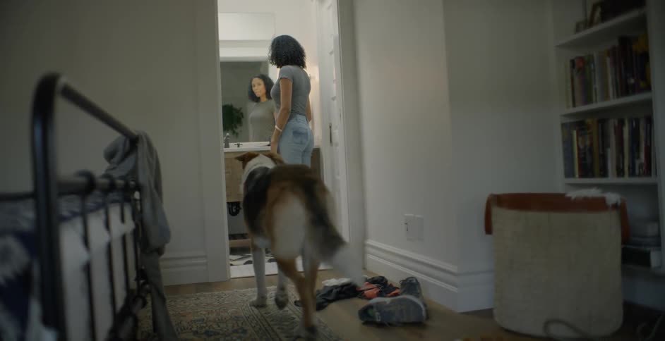 Woman is standing in front of mirror in bathroom when dog walks in
