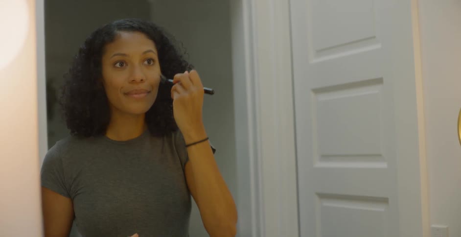 Woman is using brush to apply makeup to cheeks in front of mirror