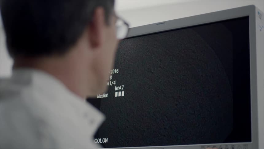 A man in a lab coat pays close attention to a monitor screen