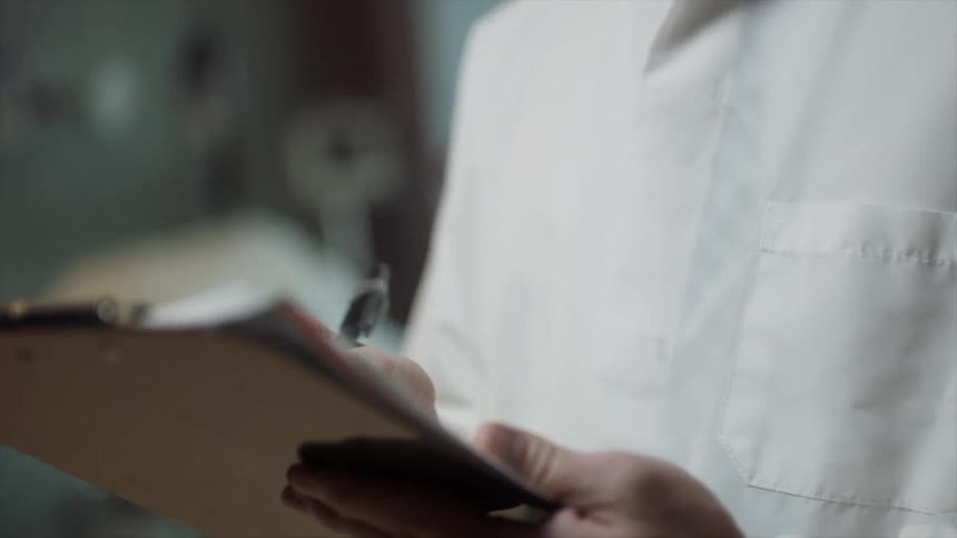 A man wearing glasses and writing on paper clipped to a clipboard