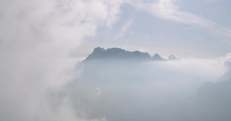 A rocky ridge becomes visible through the white clouds