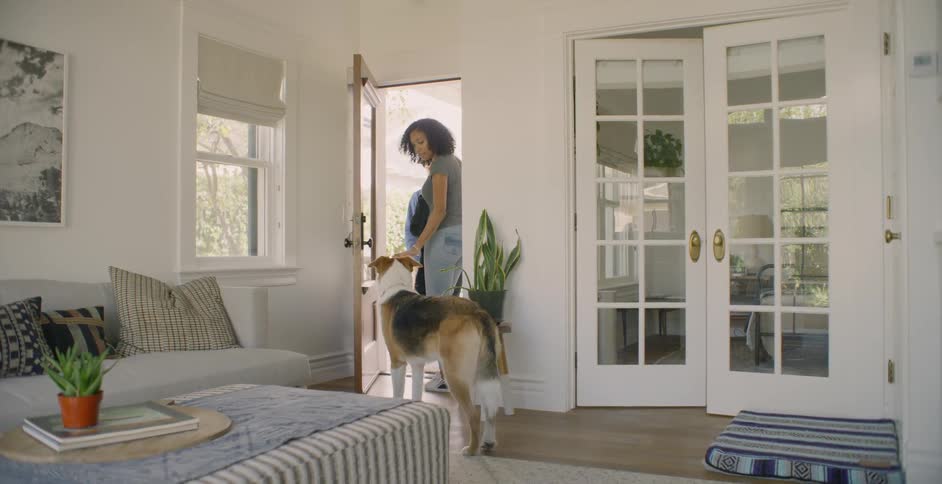 A woman grabs her jacket then leaves through the front door leaving her dog behind