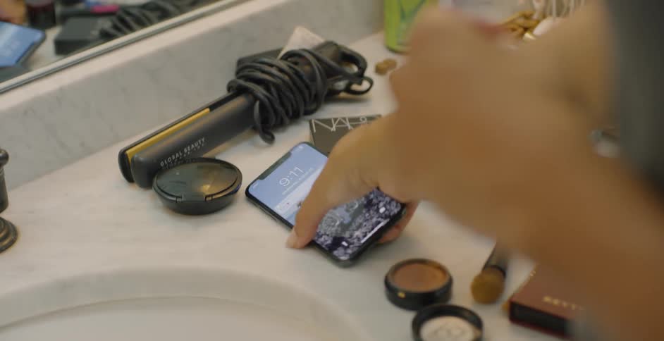 Woman picks up her cellphone as she stands at the bathroom sink