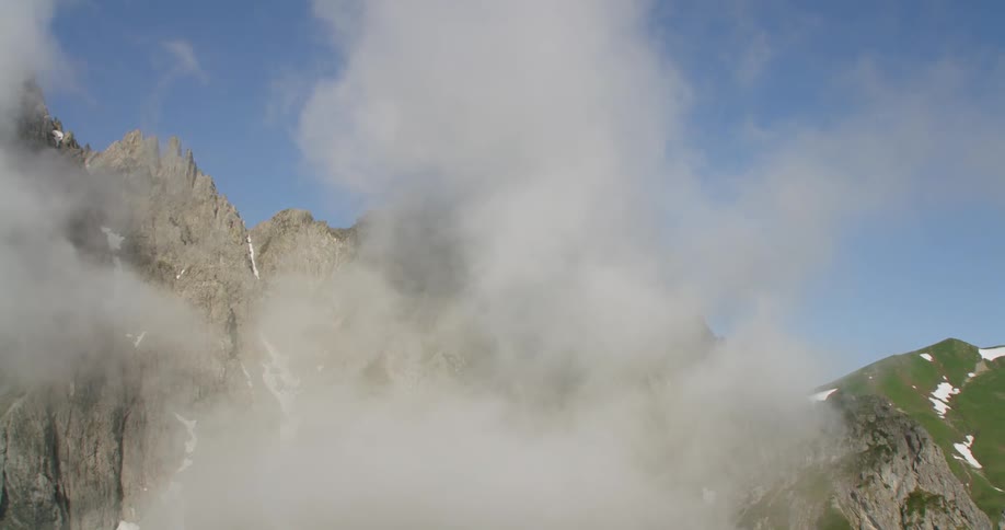 Clouds hang over rocky mountain peaks and slopes
