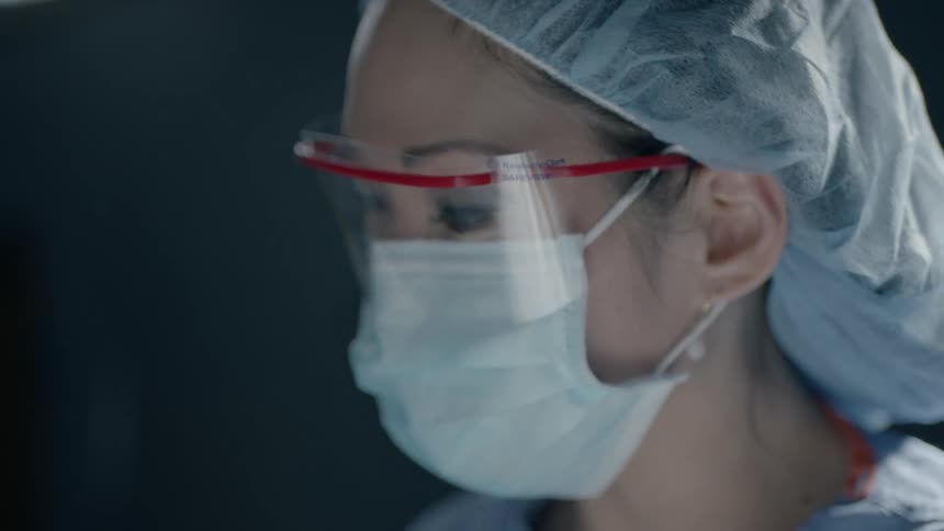 A doctor wearing a surgical mask and glasses looks on