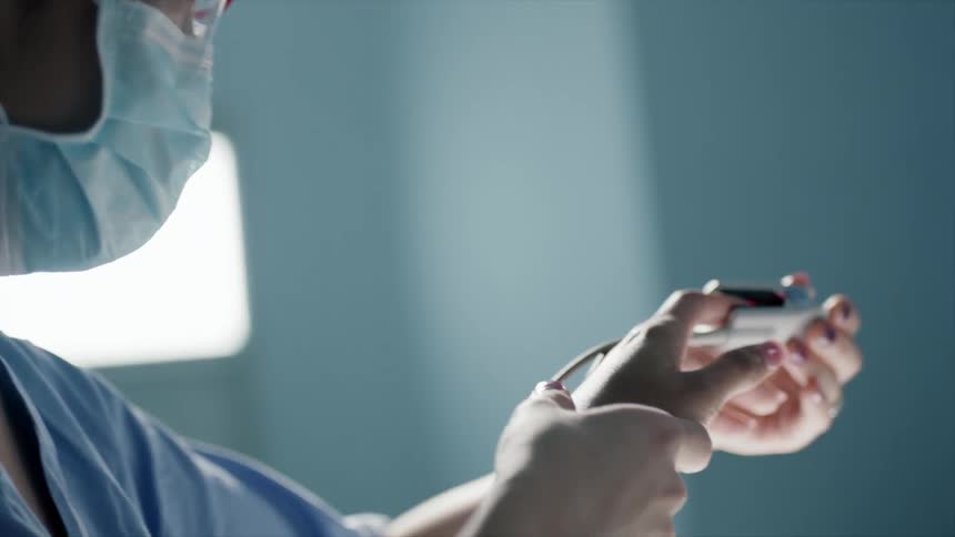 A nurse in scrubs mask and goggles places a pulse oximeter on a patients finger