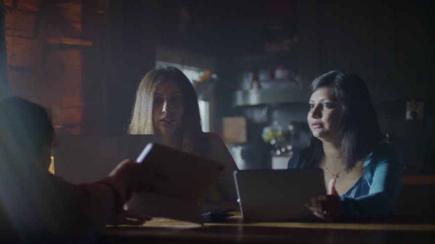 The women talk together and use computers at the dining room table