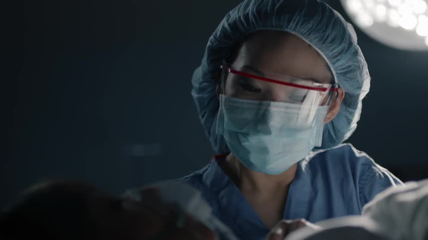 A woman wearing a surgical mask closely examines something on the patients face