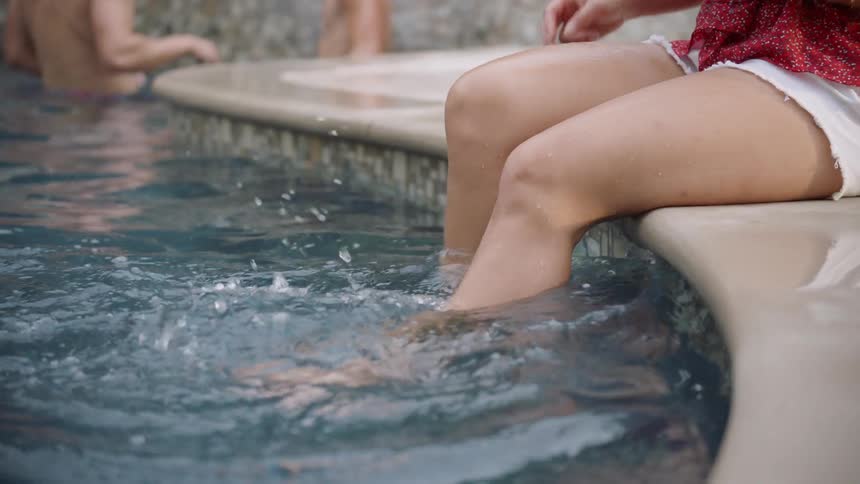 Woman kicks her legs in the pool while sitting outside of it
