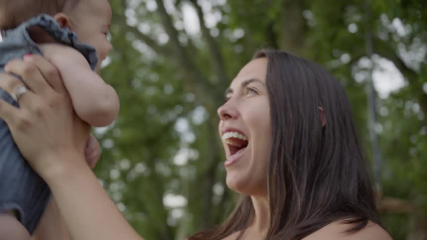 Mother is smiling and lifting baby into the air