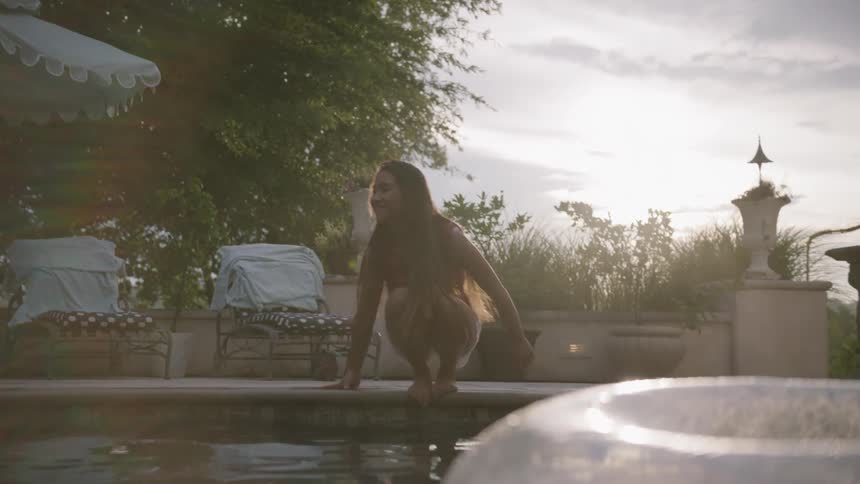 A woman is running over to a pool and putting her feet in the water in daylight