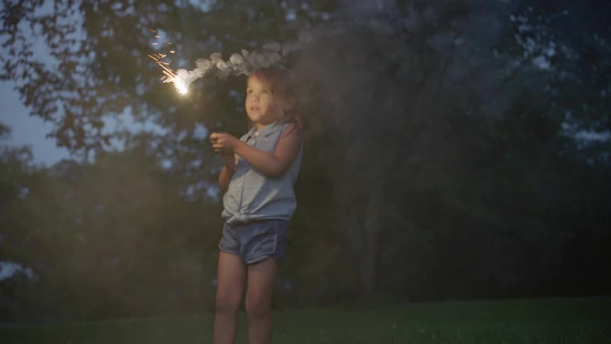 A little girl is waving a sparkler outside at dusk