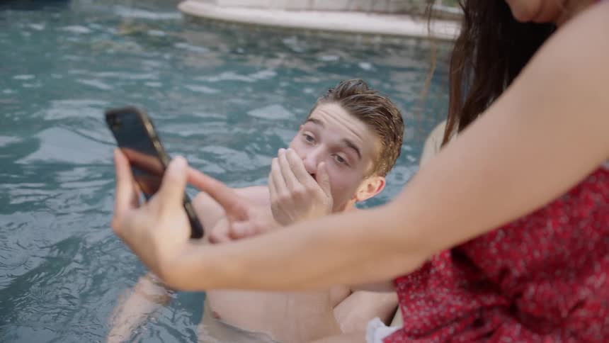 Teenage boy in a pool smiles at a picture a girl shows him