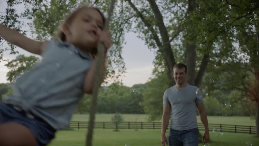 Man pushes a child on a swing while bubbles float in the air