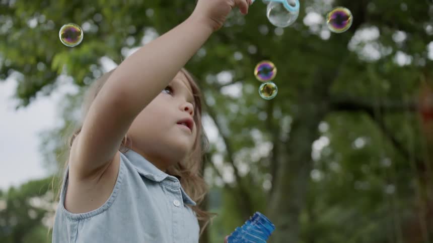 Child blows bubbles outside in the yard