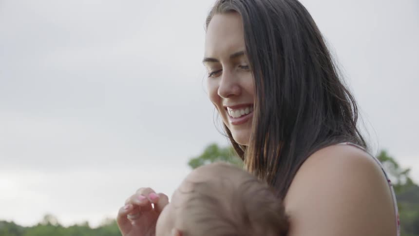 The woman smiles holding her baby in the yard