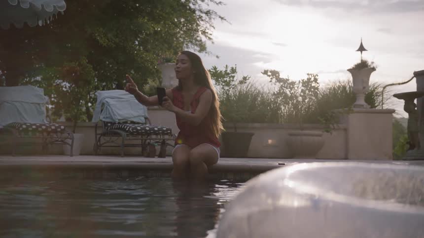 Girl sits with her legs in a pool taking a picture