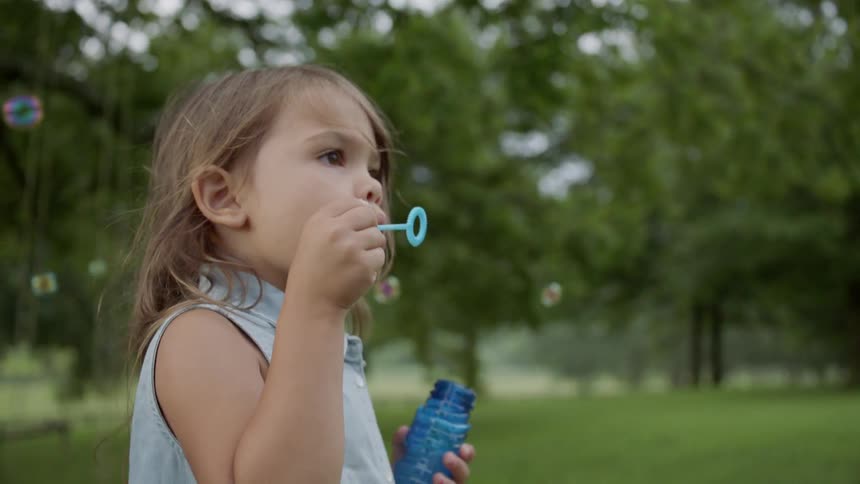 Child blows bubbles outside in the yard