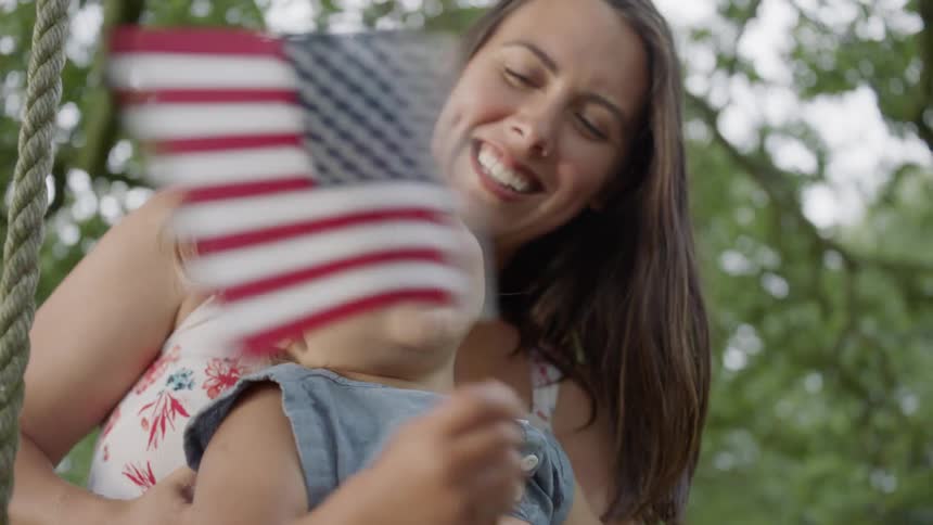 Woman smiles and hugs a toddler who is waving a flag