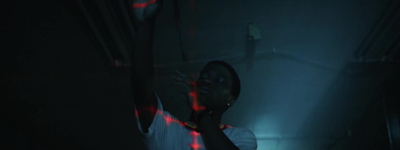 A man reaches out into the air as he stands in a room with flickering lights with his eyes closed