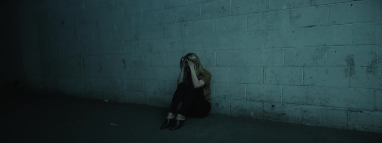 Woman sits against the brick wall as a light flashes on her