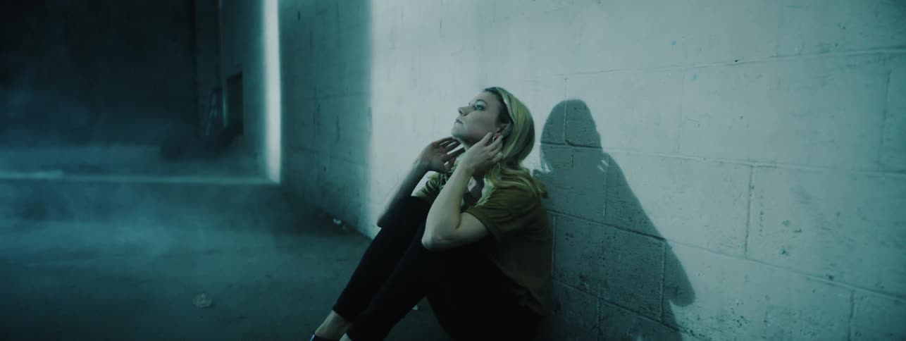 A sad woman leans against a cinder block wall