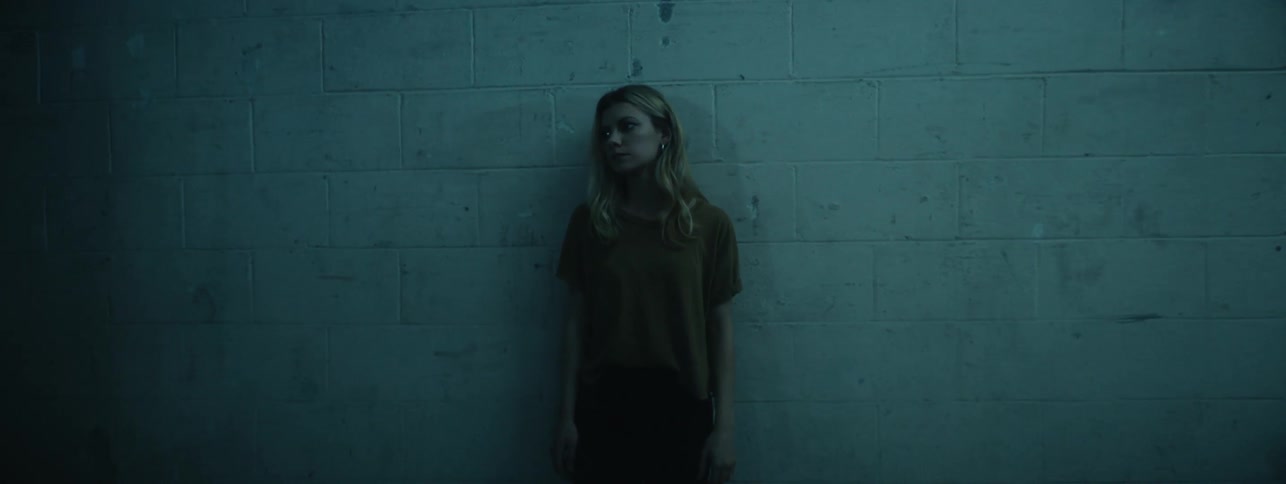 The woman is leaning against the wall in the dark room