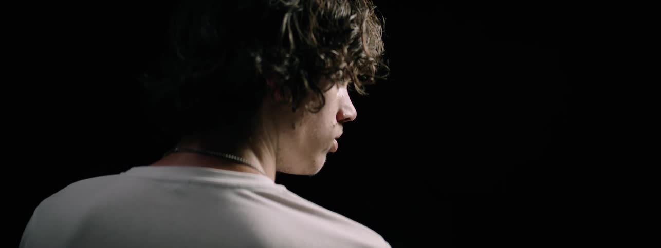 A boy in a white tee shirt lifts his head slightly and looks to the side