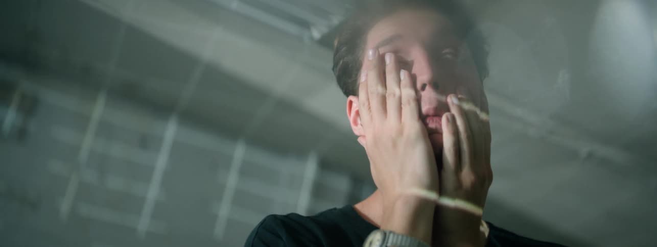 A man is rubbing and pulling at his face indoors in daylight