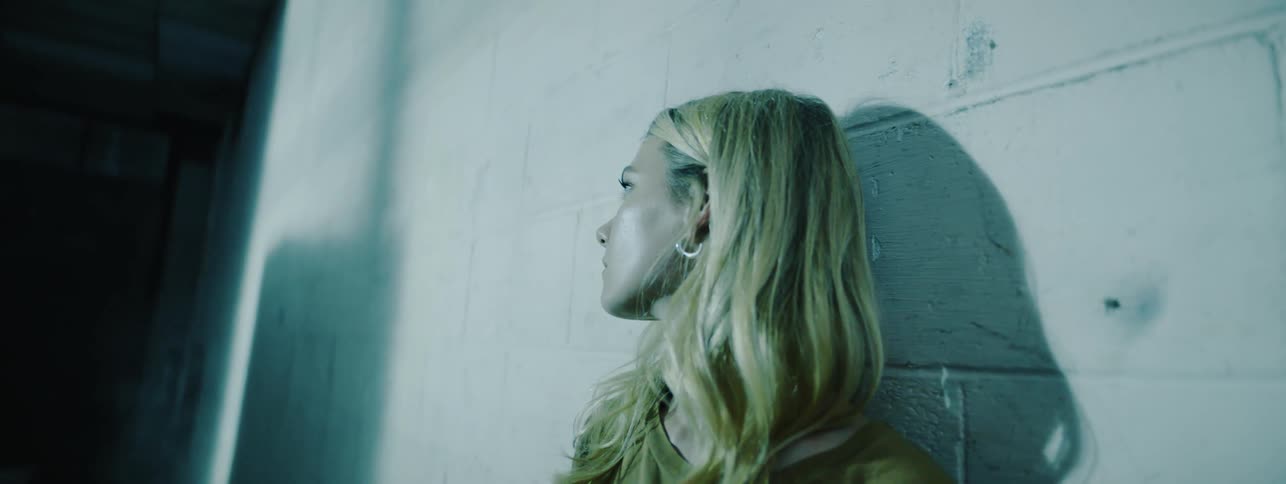 The woman leans against the wall in the dark hall