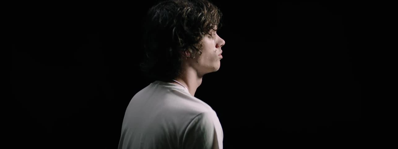 A boy in a white tee shirt sits in a black room with his eyes closed