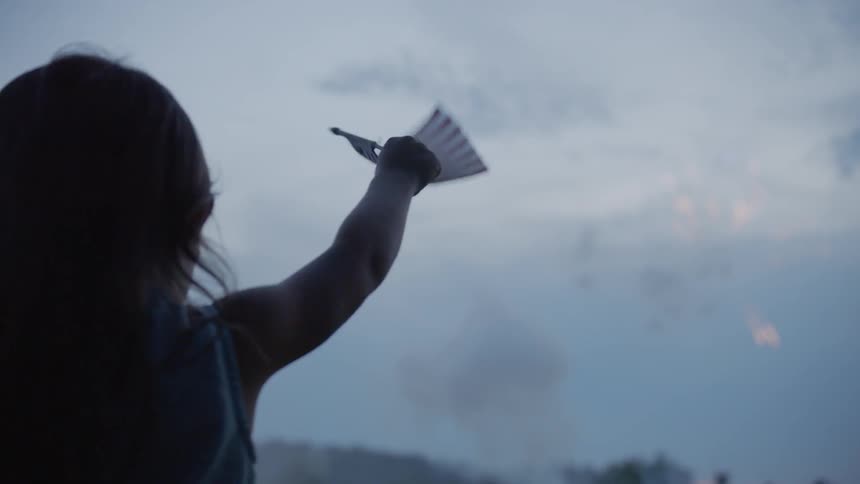 A girl waves a small american flag as she watches fireworks