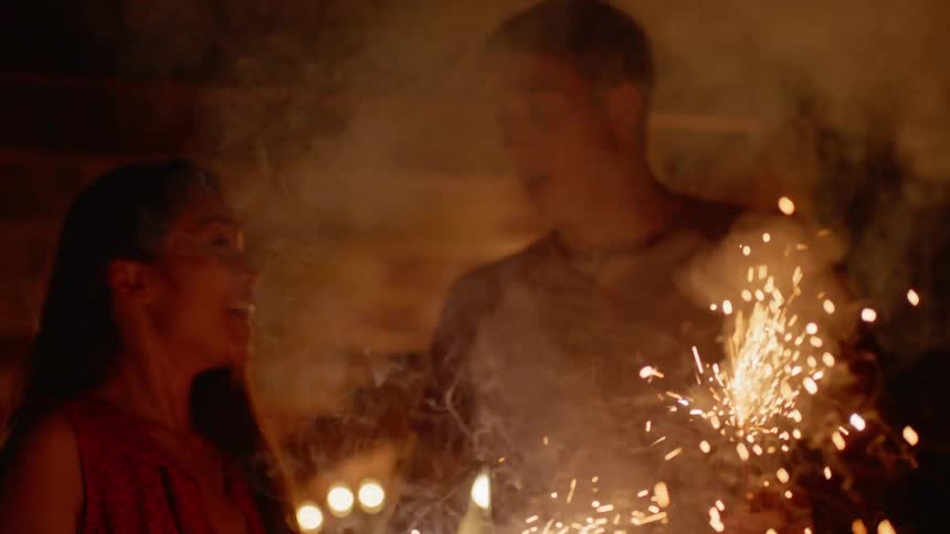 Teenage boy and girl smile and play with sparklers outside at night