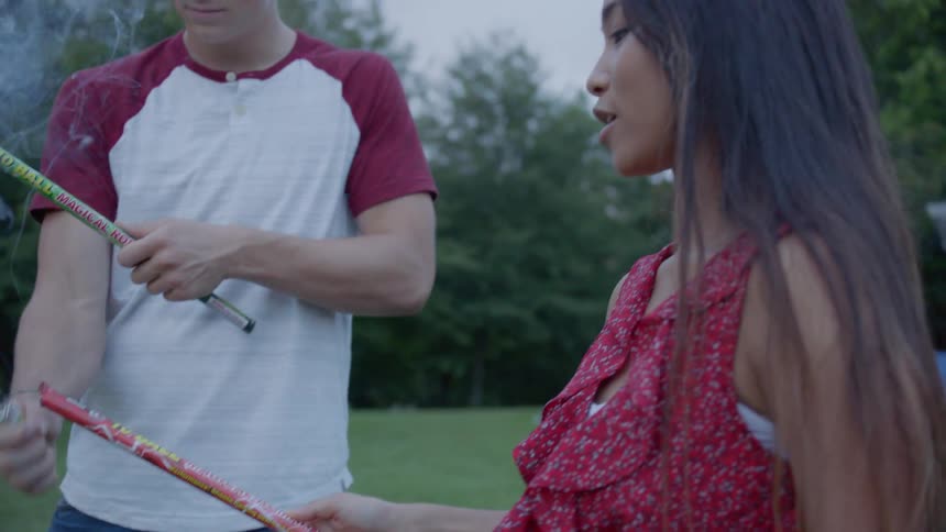A boy uses a lighter to light his and his girlfriend's sparklers