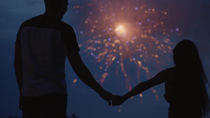 A couple holds hands as they watch fireworks