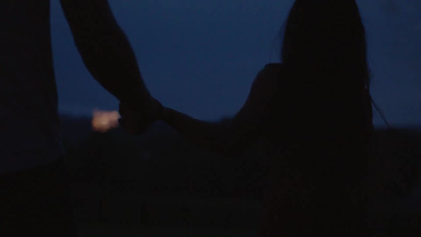 Boy and girl hold hands and watch fireworks at night