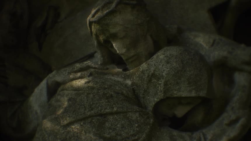 Sunlight shines on a stone statue of a man comforting a woman