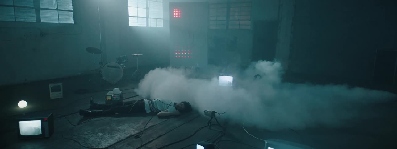 Mist floats over a  man as he lays on the floor with wires wrapped around him