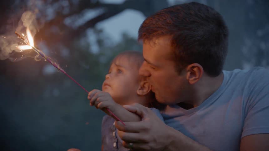 The man holds a child as they hold a sparkler