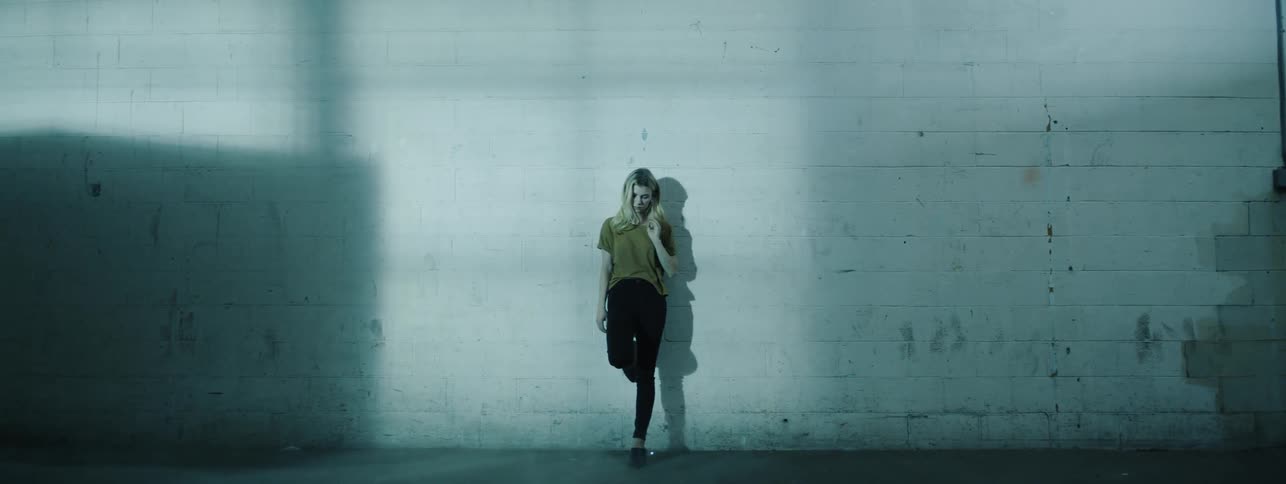 The woman brushes her hair leaning against the wall